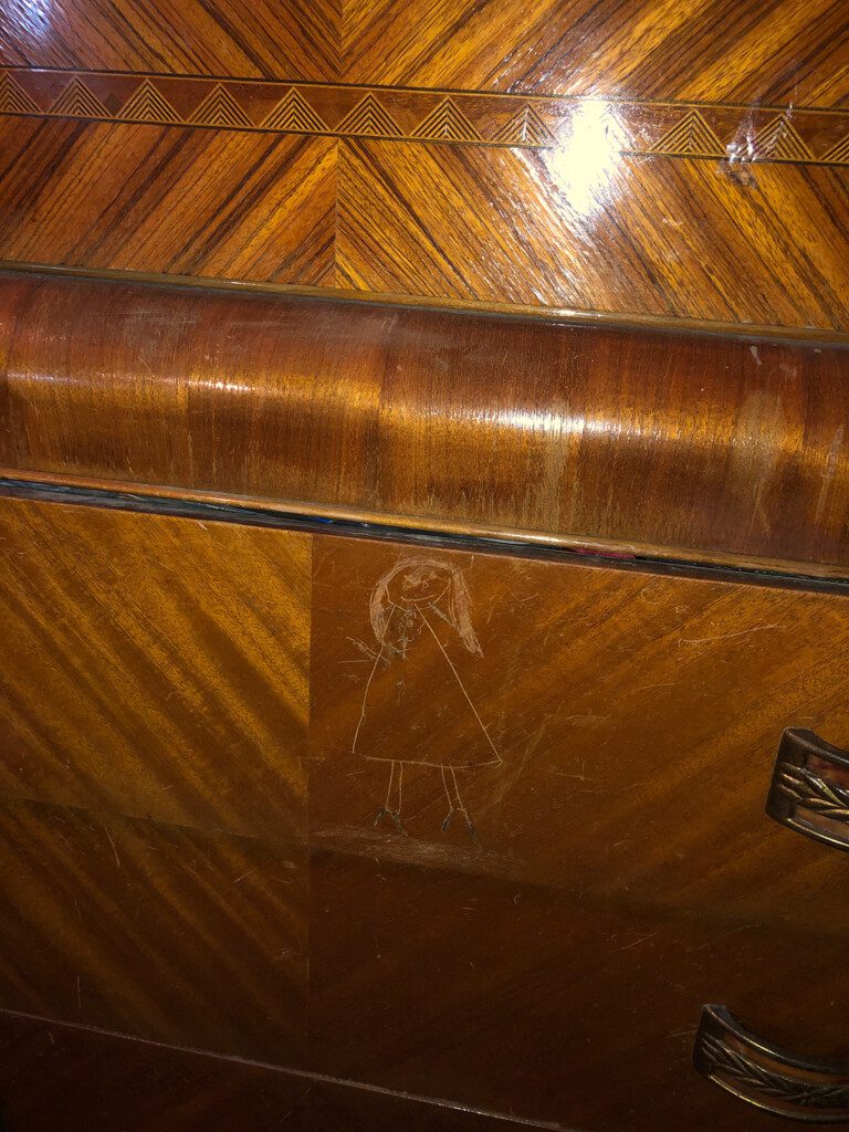 Crude drawing of a stick woman etched into a vintage, wooden dresser.