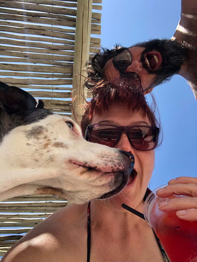 Carol, Josh and Mucca dog, shot from underneath looking up at the blue Adriatic Sky in Senigallia Italy with a campari spritz in hand.
